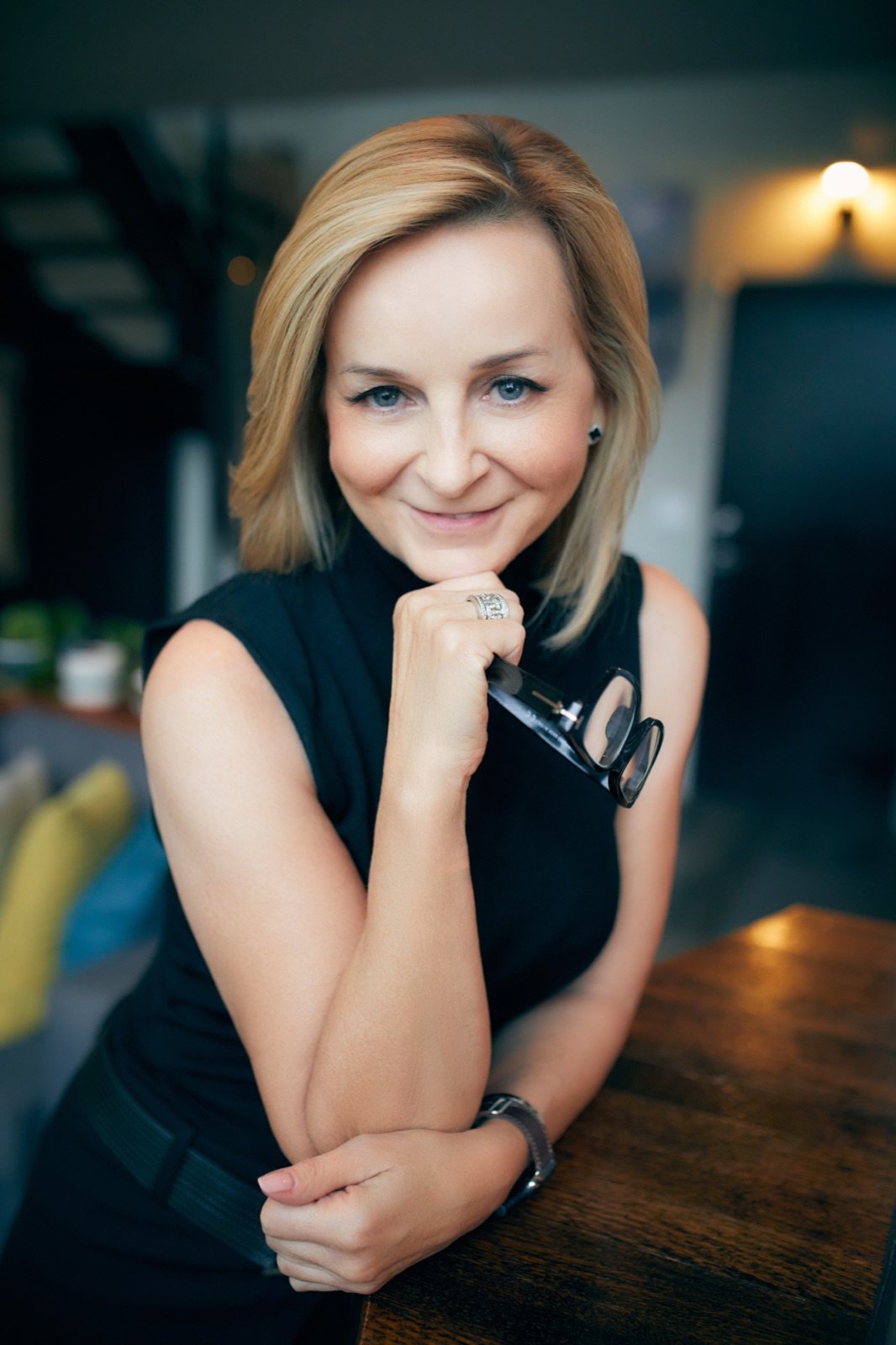 Tracy Quinton in a sleeveless black top, leaning on her arm at a walnut table