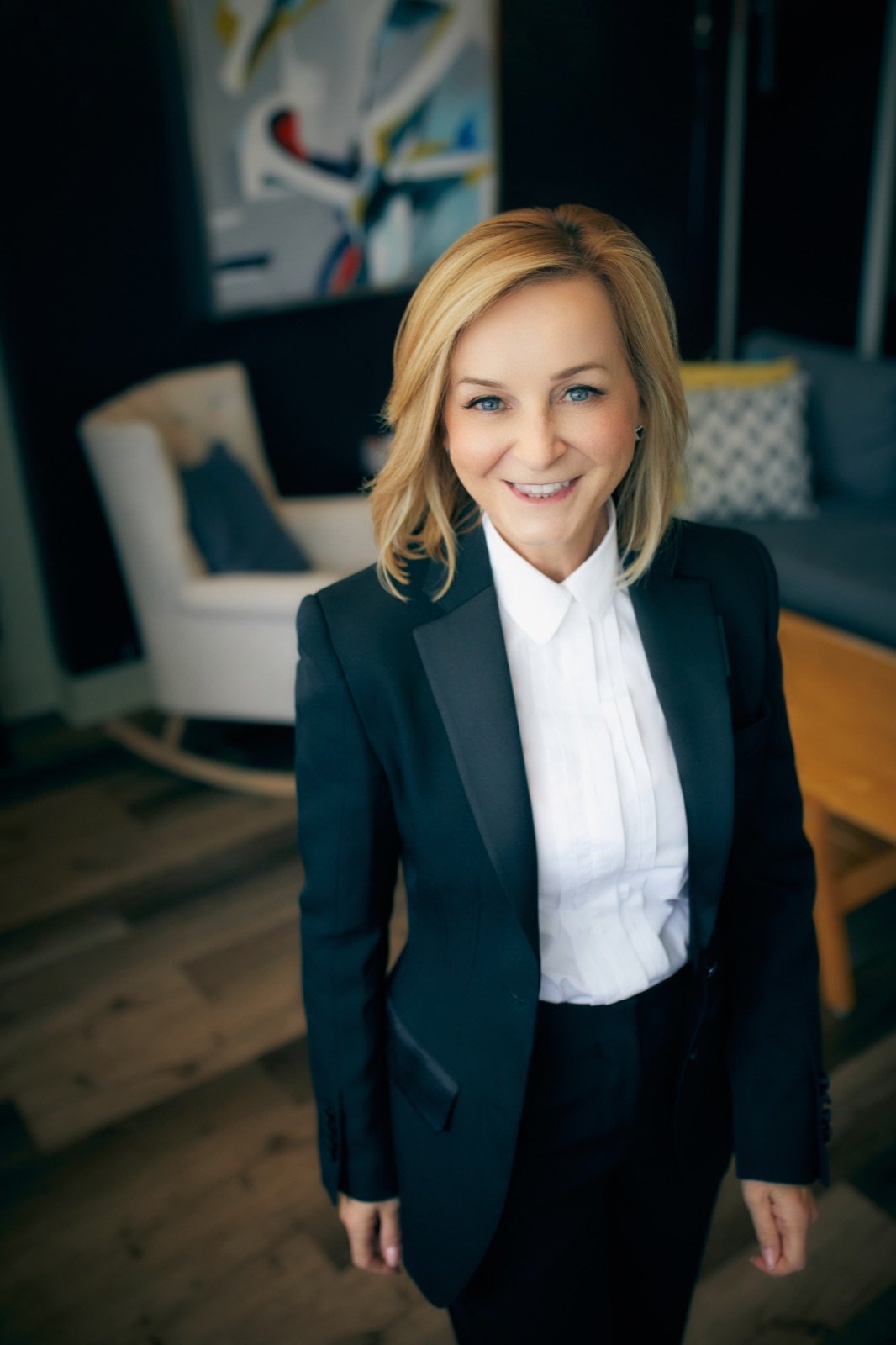 Tracy Quinton standing in a navy tuxedo suit, smiling, in a warmly lit studio