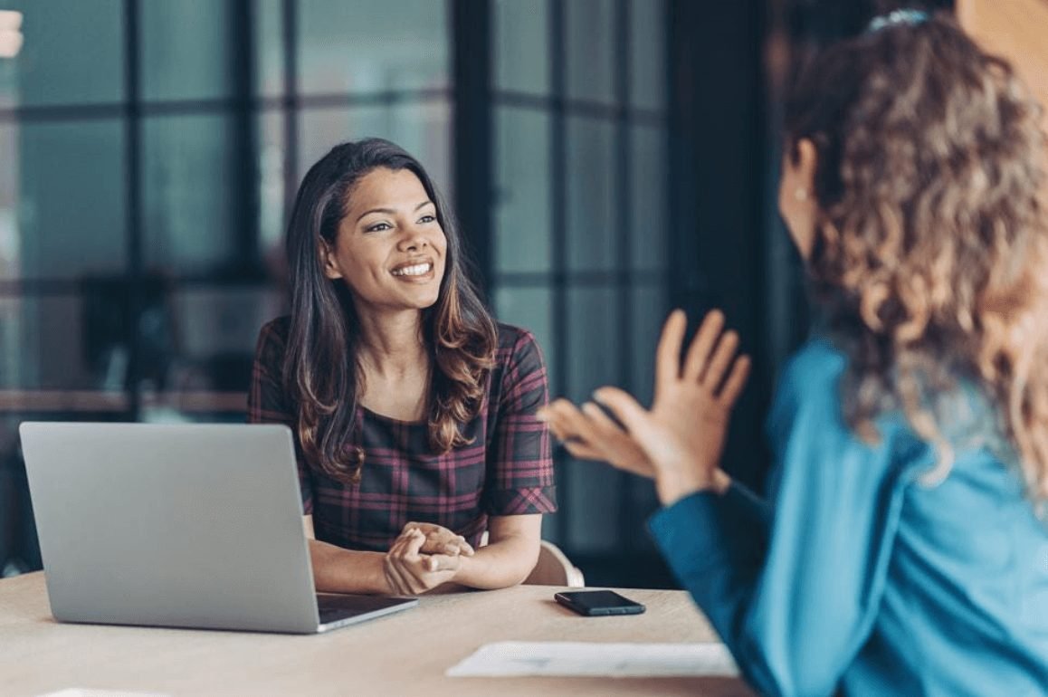 Two women in conversation at a table with a laptop